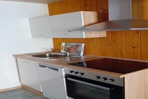 A compact kitchen with a dishwasher, oven, and a stainless steel range hood. - Gemütlicher Doppelbungalow mit Terrasse am Granzower See (Granzow)