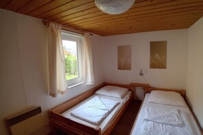 A small, single-room accommodation with a wooden ceiling, a window with curtains, and two single beds. - Gemütlicher Doppelbungalow mit Terrasse am Granzower See (Granzow)