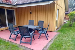 Eine Terrassengruppe mit Tisch und Stühlen, eine Holzverkleidung und eine Rasenfläche.