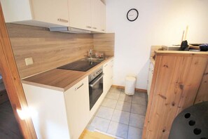 A compact kitchen with a stove, sink, and cabinets. - Skandinavischer Doppelbungalow mit Terrasse im Ferienpark Mirow (Granzow)