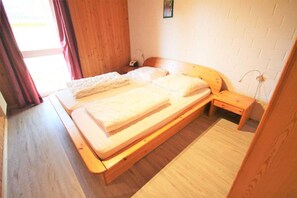 A wooden bed with a mattress and pillows, a wooden bedside table, and a wall with a white brick pattern. - Skandinavischer Doppelbungalow mit Terrasse im Ferienpark Mirow (Granzow)