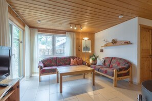 A living room with two sofas, a coffee table, a TV, and a wooden ceiling. - Doppelbungalow im skandinavischen Stil mit Terrasse im Ferienpark Mirow (Granzow)