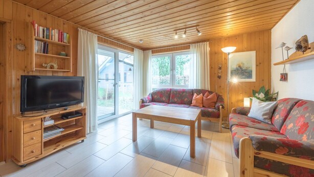 Ein Zimmer mit Holzwandverkleidung, einem Flachbildfernseher, einer Couch, einem Couchtisch und einem Bücherregal.