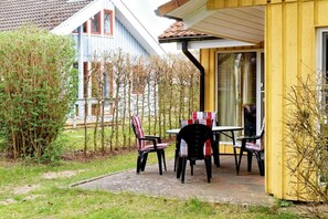 A patio with outdoor seating, a wooden building, and a blue house in the background. - Doppelbungalow im skandinavischen Stil mit Terrasse im Ferienpark Mirow (Granzow)
