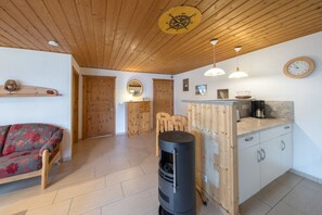 A cozy room with a sofa, a wooden ceiling, a stove, and a kitchen area with a clock. - Doppelbungalow im skandinavischen Stil mit Terrasse im Ferienpark Mirow (Granzow)