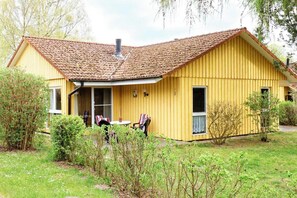 Ein gelbes Gebäude mit einem geneigten Dach, einem Schornstein und einer kleinen Veranda mit Tisch und Stühlen.