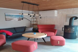 Ein modernes Wohnzimmer mit einer Couch, Sesseln, einem runden Tisch und einem Kaminofen.