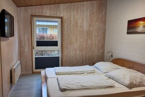 Ein Schlafzimmer mit zwei Betten, einem Fenster mit Jalousien, einem Heizkörper und einem Bild an der Wand.