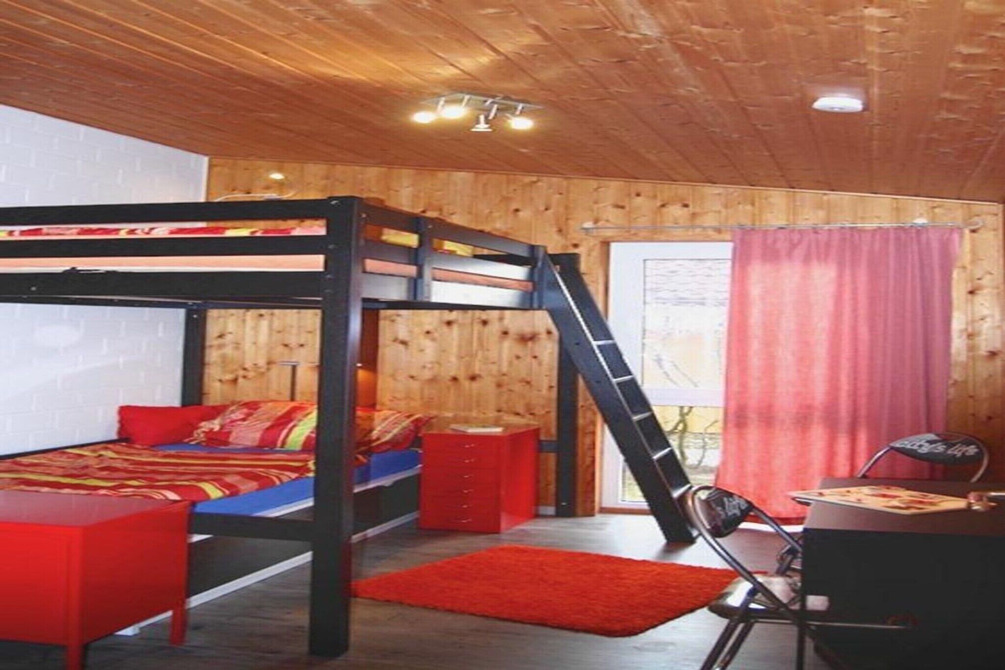 A bunk bed room with a desk and chair, wooden walls, and a window with curtains.
