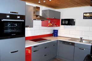 A kitchen with a built-in oven, microwave, and red cabinetry. - Gemütlicher Doppelbungalow mit Terrasse und Garten im Ferienpark Mirow (Granzow)