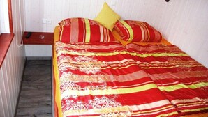 Una cama con una colcha a rayas rojas y amarillas, un cojín amarillo y una mesita de noche de madera con un teléfono.
