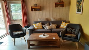 A living room with a sofa, two armchairs, a coffee table, wooden shelves, and a window with curtains. - Double bungalow in country house style with terrace in the Mirow holiday park (Granzow)