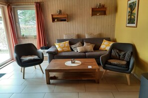 A living room with a sofa, two armchairs, a coffee table, wooden shelves, and a window with curtains. - Double bungalow in country house style with terrace in the Mirow holiday park (Granzow)
