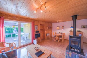 A wooden interior with a dining area, a fireplace, and a sliding glass door leading to an outdoor seating area. - Geräumiger Doppelbungalow mit Terrasse und Garten im Ferienpark Mirow (Granzow)