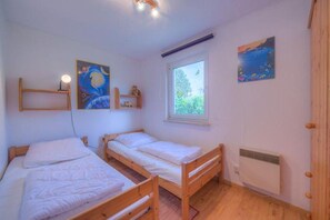A room with two wooden bunk beds, a window with a view of greenery, and a radiator. - Geräumiger Doppelbungalow mit Terrasse und Garten im Ferienpark Mirow (Granzow)