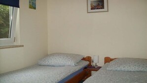 Quarto com duas camas de solteiro, uma janela, um quadro na parede e uma mesinha com abajur.
