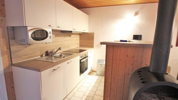 Uma cozinha compacta com armários brancos, micro-ondas, pia, forno e lareira a lenha.