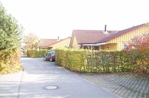 Eine Wohnstraße mit Häusern, einem am Straßenrand geparkten Auto und einem Straßenabdeckel.