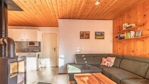 Ein gemütlicher Wohnbereich mit einer Couch, einem Holztisch, einer Küche mit Mikrowelle und einem Kaminofen.