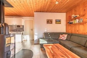 Ein gemütlicher Wohnbereich mit einer Couch, einem Holztisch, einer Küche mit Mikrowelle und einem Kaminofen.