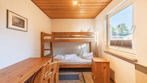 Ein Schlafraum mit Etagenbetten, einem Holztisch und Stuhl, einem gerahmten Bild an der Wand und einem Fenster mit Blick auf Bäume.