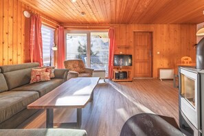 A cozy cabin interior with a sofa, a wooden table, a television, and a fireplace. - Familienfreundlicher Doppelbungalow mit Terrasse in Mirow (Granzow)