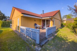 A single-story house with a red-tiled roof, a fenced porch with a table and chairs, and a small garden area. - Familienfreundlicher Doppelbungalow mit Terrasse in Mirow (Granzow)