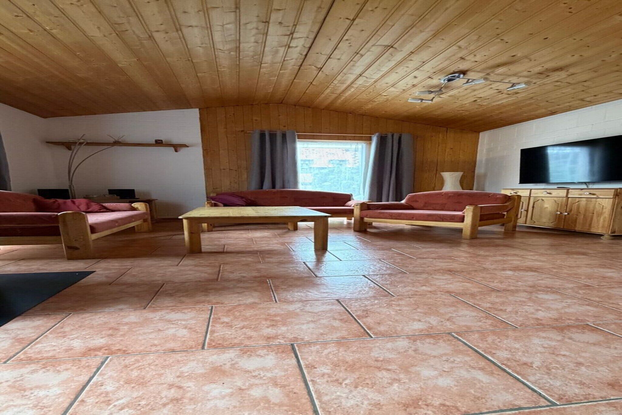 Eine Holzbalkendecke, ein Fernseher, ein Sofa, ein Tisch und ein Fenster mit Vorhängen.