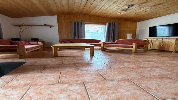 Techo de madera, televisor, sofá, mesa y ventana con cortinas.