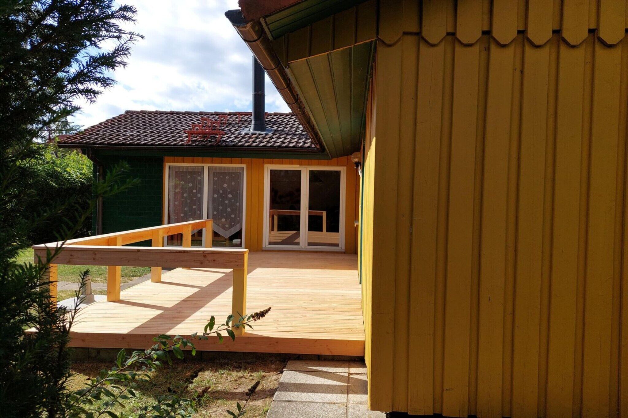 A wooden deck with a railing, a green building with a tiled roof, and a yellow structure with vertical siding.