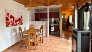 Un interior de madera con una mesa y sillas de comedor, una cocina con armarios rojos y un estufa de leña.