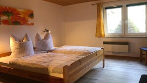 Un dormitorio con una cama de madera, una mesita de noche, una ventana con cortinas y un radiador.