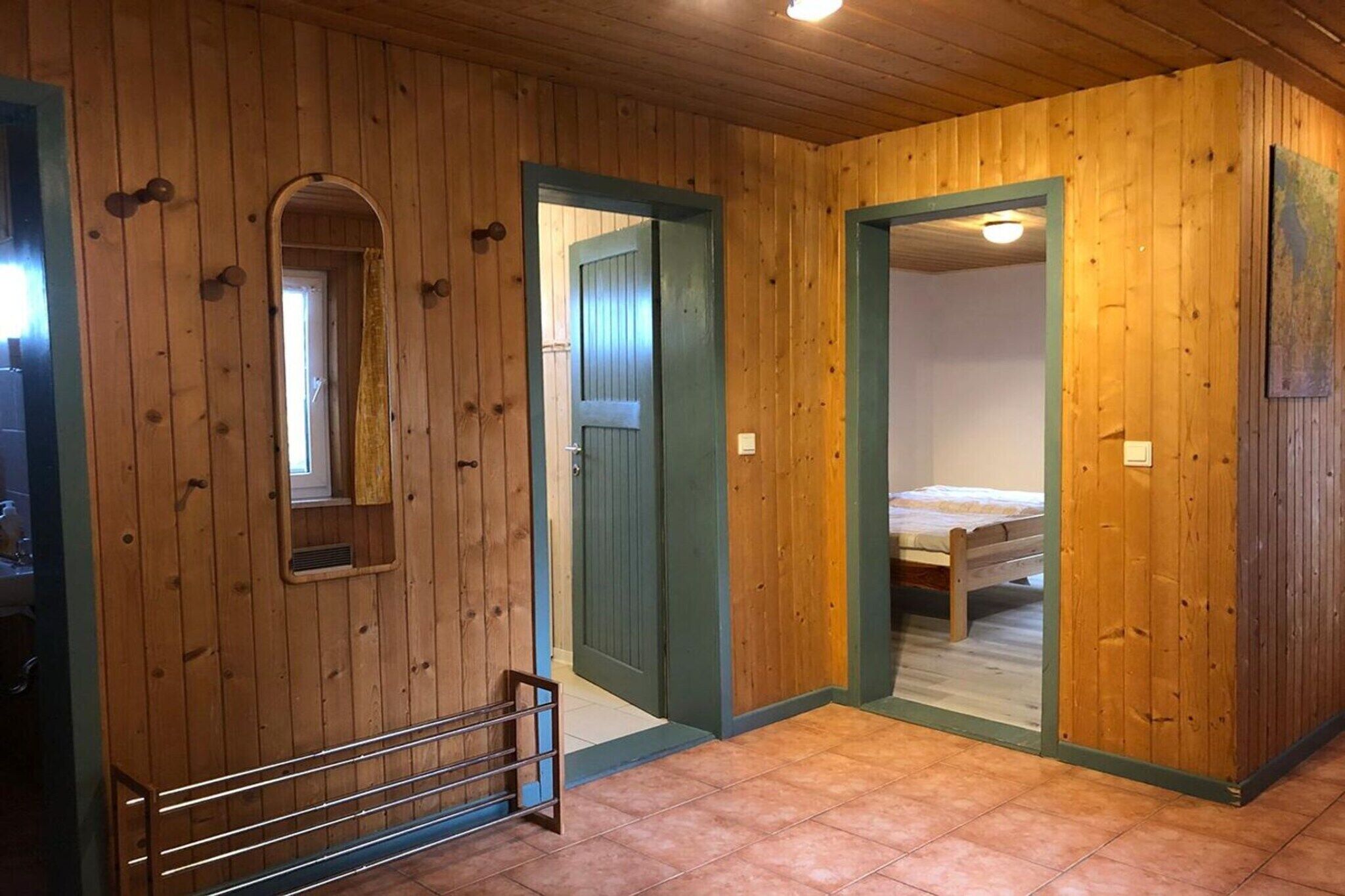 A wooden interior with a bed, a window, and a door leading to another room.