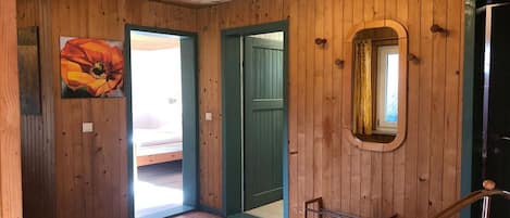 Un intérieur en bois avec une porte donnant sur un balcon, une rambarde en métal et un tableau encadré au mur.