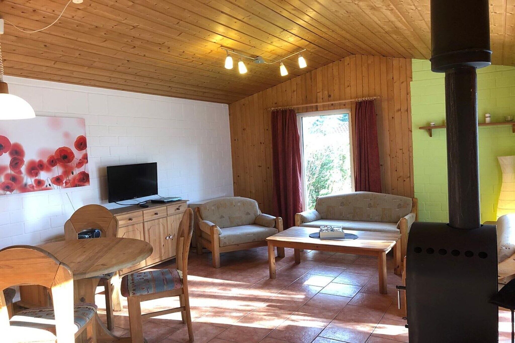 A wooden interior with a TV, sofa, dining table, chairs, and a wood stove.