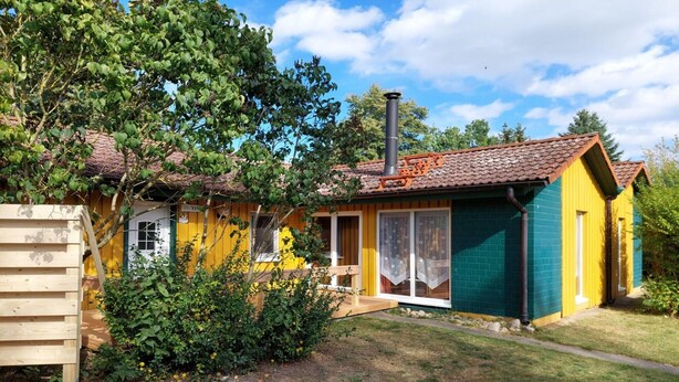 Une maison à deux étages avec une cheminée bien visible, une clôture en bois et un jardin.