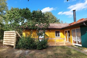 A yellow building with a chimney, a wooden structure, and a small window. - Komfortabler Doppelbungalow mit Terrasse im Ferienpark Mirow (Granzow)