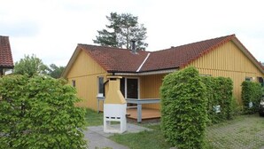 Ein gelbes Gebäude mit rotem Ziegeldach, einer Veranda und einer kleinen weißen Struktur davor.