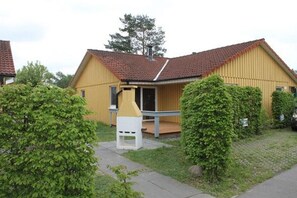 Ein gelbes Gebäude mit rotem Ziegeldach, einer Veranda und einer kleinen weißen Struktur davor.