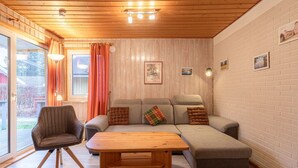 Ein gemütliches Wohnzimmer mit Holzbalkendecke, einer Sofagarnitur, einem Holztisch und einem Sessel.