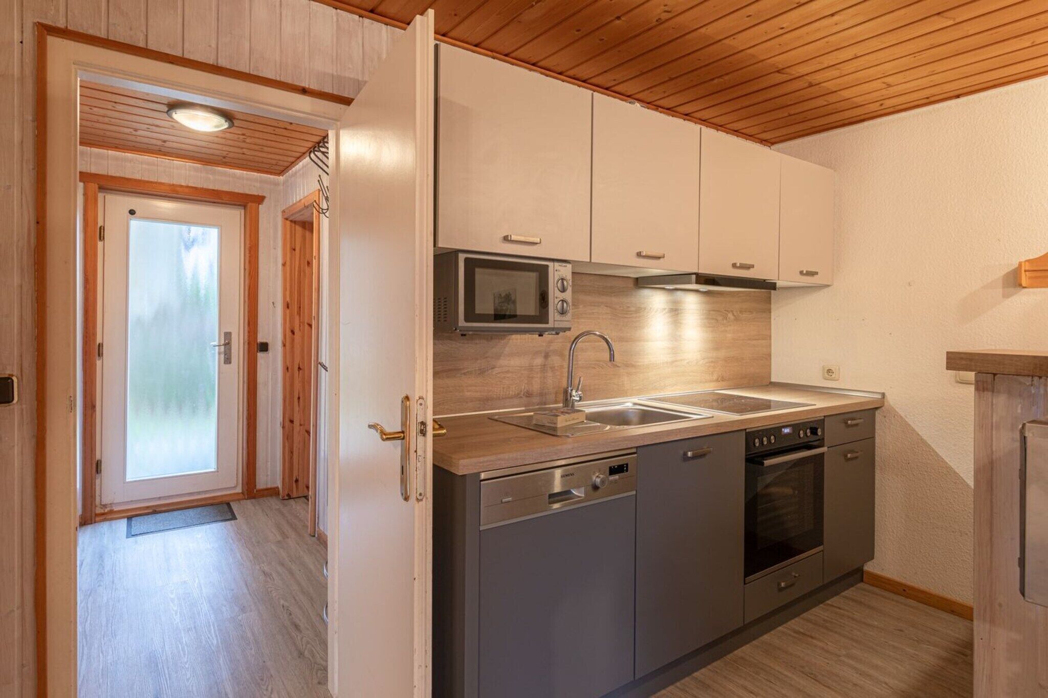 A modern kitchen with stainless steel appliances, wooden flooring, and a wooden ceiling.