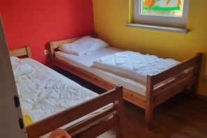 A room with two wooden beds, a red wall, a yellow wall, and a window with a view of a green landscape. - Gemütlicher Doppelbungalow im Ferienpark Mirow mit Terrasse (Granzow)
