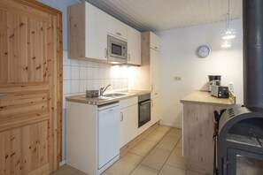Eine kompakte Küche mit weißen Schränken, einer Mikrowelle, einem Geschirrspüler, einem Backofen, einer Spüle und einer Kaffeemaschine.