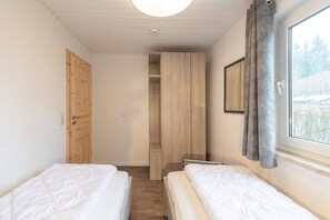 Ein Schlafzimmer mit zwei Betten, einem Holzschrank, einem Fenster mit Vorhängen und einer Tür.