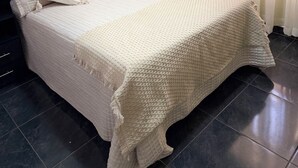 Una cama con manta texturizada, cabecera oscura y varias almohadas.