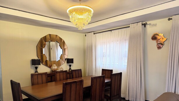 Un comedor con una larga mesa, sillas, un candelabro, un espejo grande y una ventana con cortinas.