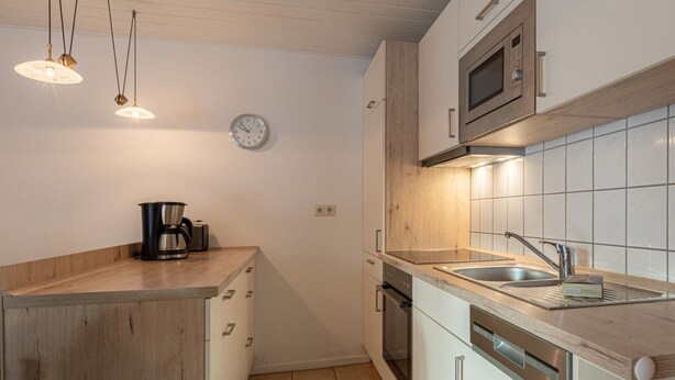 Eine moderne Küche mit Holzschränken, einem eingebauten Backofen, einer Mikrowelle, einer Spüle und Pendelleuchten.