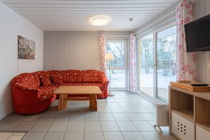 A living room with a red sofa, a wooden coffee table, a TV on the wall, and a window with curtains. - Gemütlicher Doppelbungalow mit Garten und Terrasse im Ferienpark Mirow (Granzow)