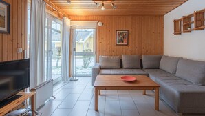 Ein modernes Wohnzimmer mit Holzboden, einem großen Sofa, einem Couchtisch, einem Fernseher und einer Glastür zum Garten.