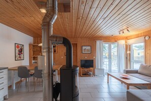 Een knus interieur van een chalet met een houtkachel, een eethoek, een bank en een televisie.